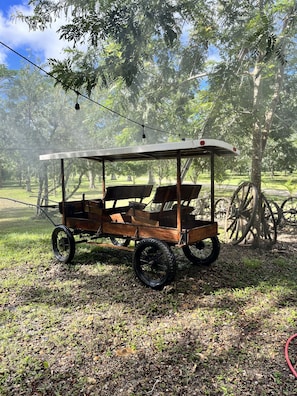 Un carruaje de madera con banca, rodeado de árboles y hierba.
