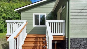 A wooden staircase leading to a deck with white railings, a window, and a stone wall. - Little Green House
Eclectic Olympic National Park Basecamp, Dogs allowed (Port Angeles)