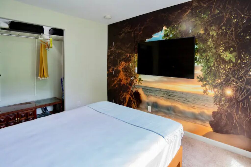 Une chambre à coucher avec un lit, un téléviseur fixé au mur et une fresque représentant une scène de plage.