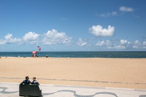 A beach with a clear sky, a lifeguard tower, and a few people in the distance.