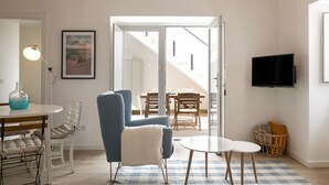 A modern living room with a blue armchair, a round table, and a television mounted on the wall. - Casa da Saudade Sunny Rooftop (Peniche)