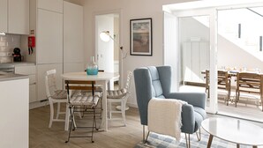 A modern kitchen with white cabinets, a dining area with a table and chairs, and a blue armchair. - Casa da Saudade Sunny Rooftop (Peniche)