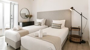 A hotel room with two beds, a bedside table, a mirror, a floor lamp, and a wicker side table. - Casa da Saudade Sunny Rooftop (Peniche)