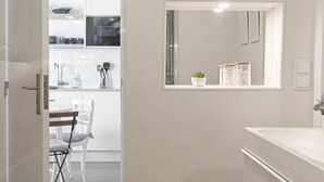 A modern bathroom with a large mirror, a sink, and a door leading to a dining area. - Casa da Saudade Sunny Rooftop (Peniche)
