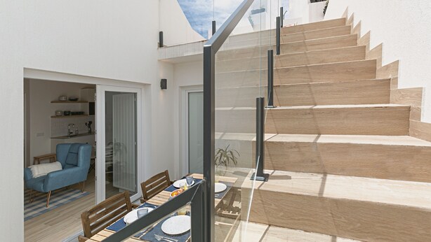 A modern interior with a staircase leading to an upper level, a dining area with a table set for two, and a blue armchair in the adjacent room. - Casa da Saudade Sunny Rooftop (Peniche)