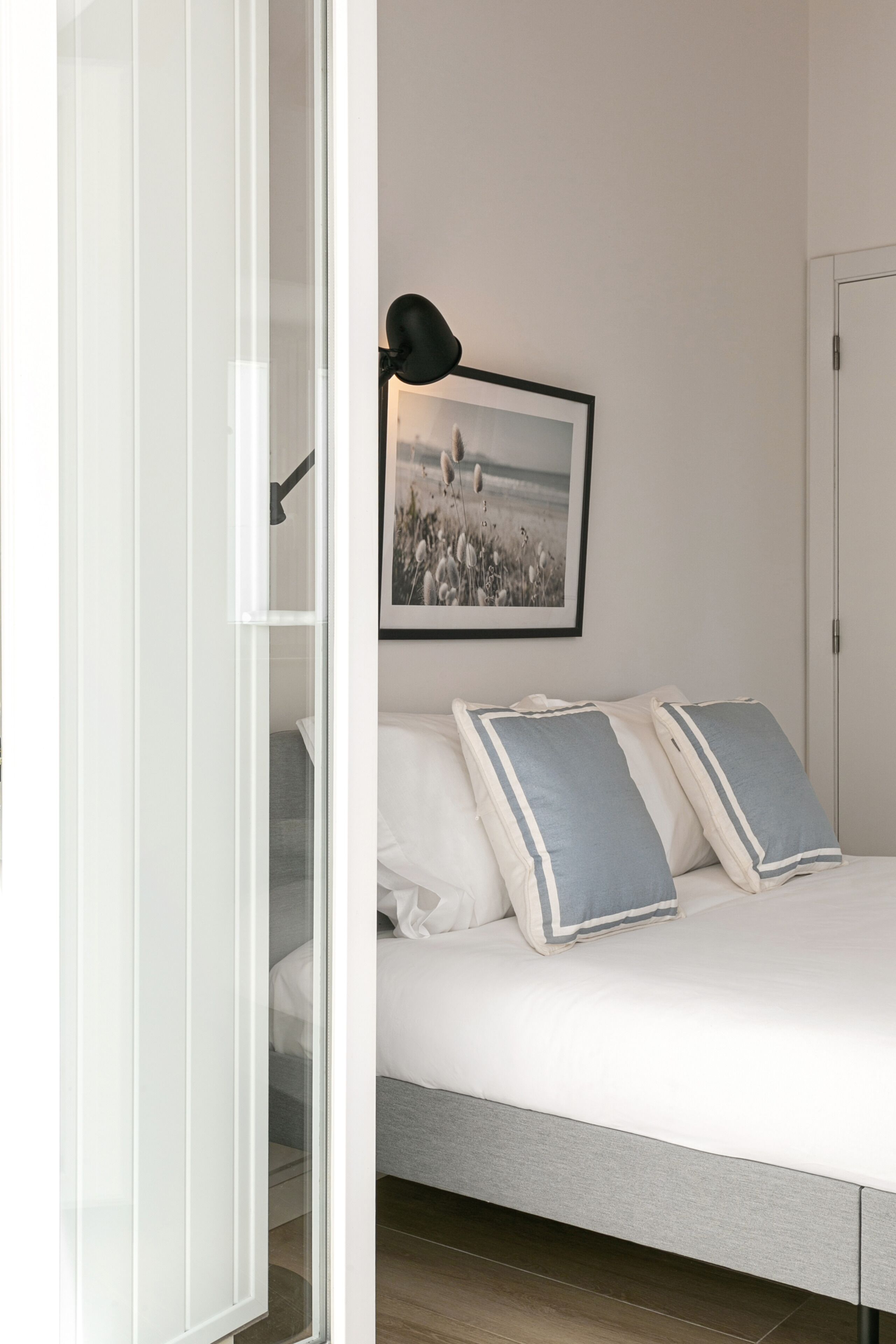 Une chambre à coucher avec un lit, des oreillers, un tableau encadré au mur et une porte.