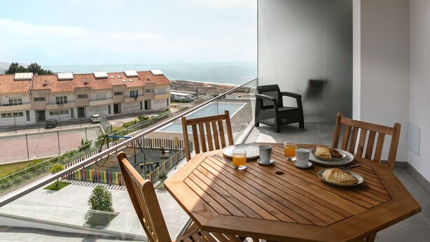 Un balcón con una mesa de madera dispuesta para el desayuno, con vistas a la costa.