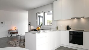 Una cocina moderna con armarios blancos, horno empotrado y un amplio ventanal que proporciona luz natural.