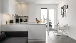Una cocina moderna con armarios blancos, una zona de comedor con sillas blancas y vistas al exterior.