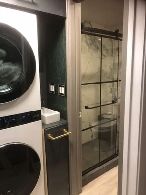 Un área de lavandería con lavadora, lavamanos y cabina de ducha de vidrio.
