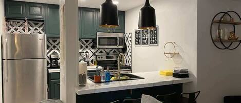 Una cocina moderna con una isla central, electrodomésticos de acero inoxidable e iluminación colgante.