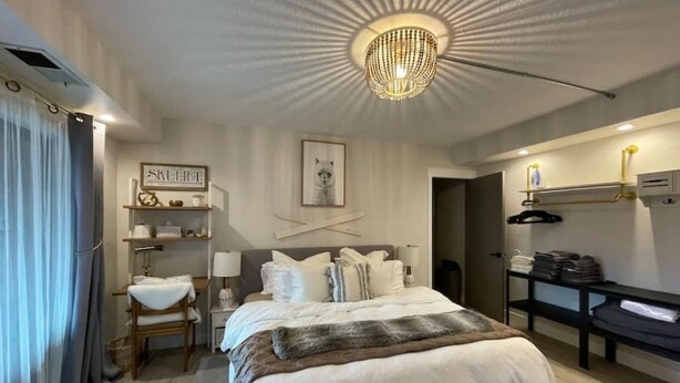 Un dormitorio con una cama grande, una araña, una mesita de noche, una silla, un armario y una estantería en la pared.