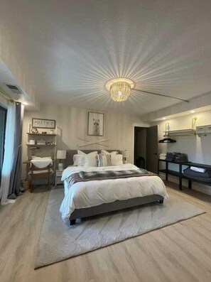 A modern bedroom with a large bed, a chandelier, a desk, and a wardrobe.