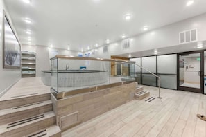 Un hall d’hôtel moderne avec une rambarde en verre, un comptoir d’accueil et un escalier menant à un étage supérieur.