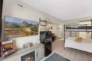 Une chambre moderne dotée d’une cheminée, d’un lit superposé, d’un téléviseur à écran plat, d’un réfrigérateur et d’un tableau représentant un paysage.