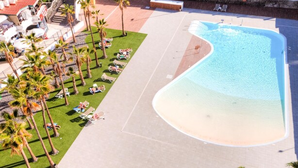 Vista aérea de un resort con una amplia piscina, palmeras y tumbonas.