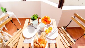 Una mesa con pan, naranjas y una planta en un balcón con sillas y vistas al exterior.