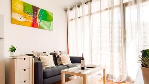 Una sala moderna con un sofá, una mesa de centro y un aparador. Hay un cuadro en la pared y una ventana con cortinas.