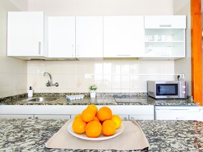 A kitchen with white cabinets, a granite countertop, a sink, a microwave, and a plate of oranges.