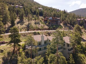 A modern two-story building with a balcony on the upper floor, surrounded by dense forest and a mountain backdrop. - Cliffview Luxury Vacation Rental at Windcliff (Estes Park)