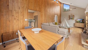 A modern kitchen with wooden paneling, a dining area with a wooden table and chairs, a sofa, and a TV in the living area. - Cliffview Luxury Vacation Rental at Windcliff (Estes Park)