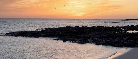 Ein Strand mit felsigem Ufer und einem Sonnenuntergang.