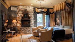 A cozy bedroom with a stone fireplace, a bed, a chandelier, and a view of the outdoors. - Twin Pine Manor Bed & Breakfast (Ephrata)