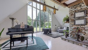 A spacious living area with a piano, a stone wall, and large windows offering a view of the outdoors. - Twin Pine Manor Bed & Breakfast (Ephrata)