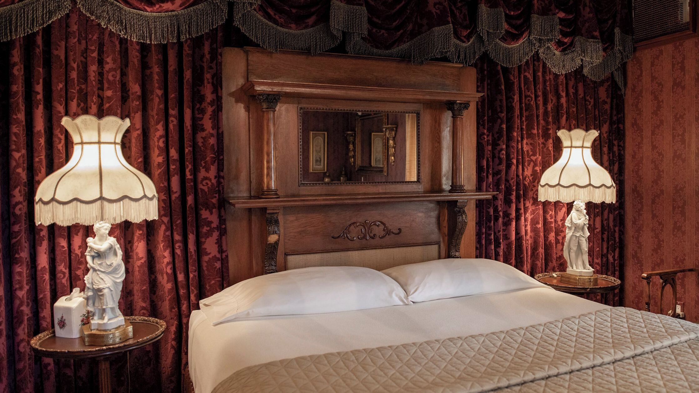 A bedroom with a large bed, ornate wooden headboard, and two lamps with fringed shades.