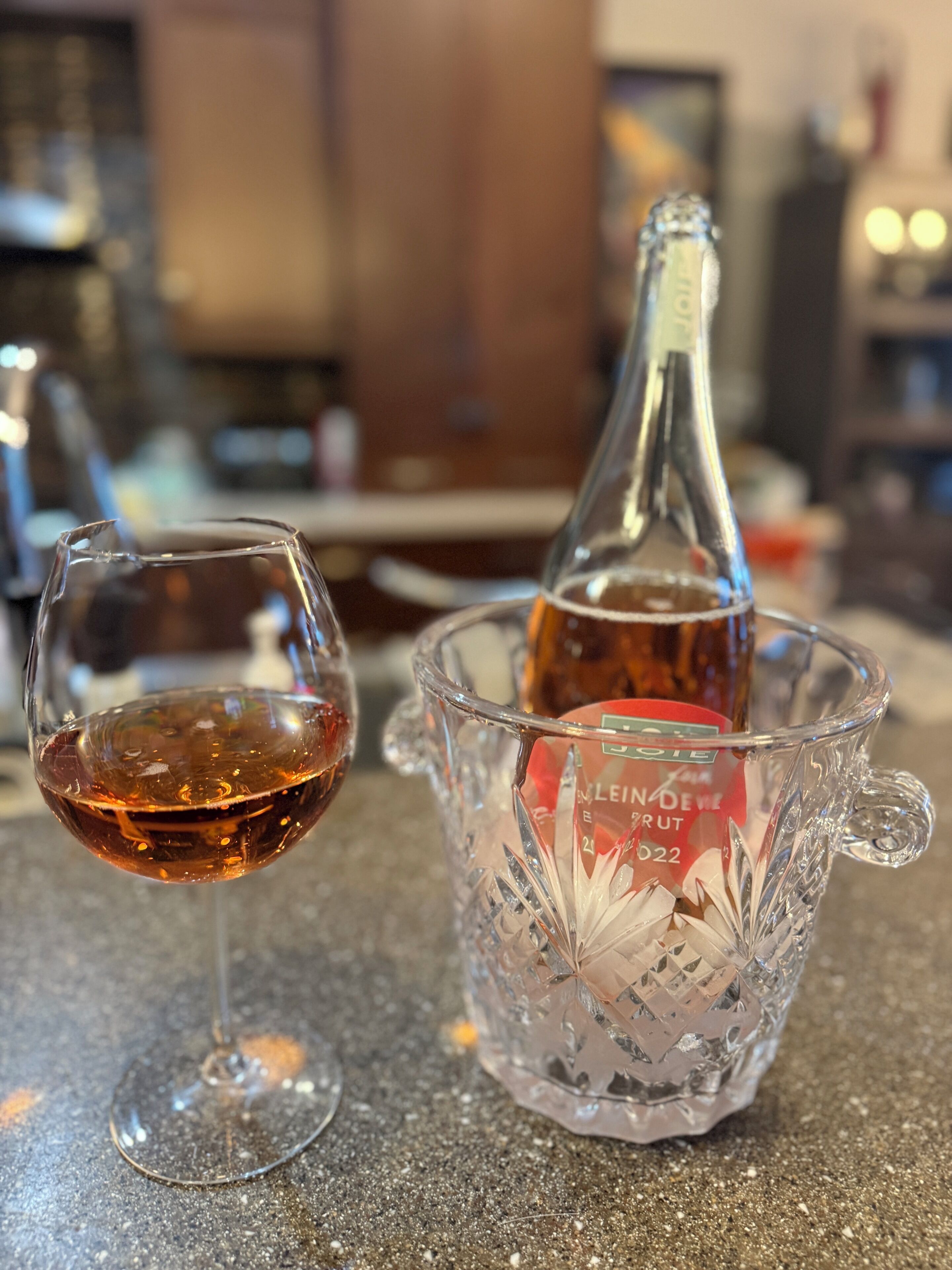 A glass of red wine and a bottle in a glass decanter on a countertop.