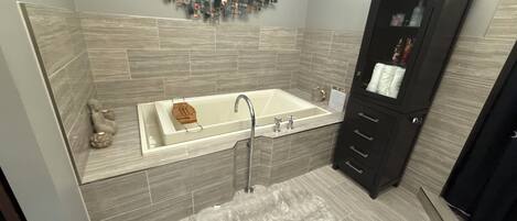 A modern bathroom with a large bathtub, a dark wooden cabinet, and a decorative wall piece above the tub.