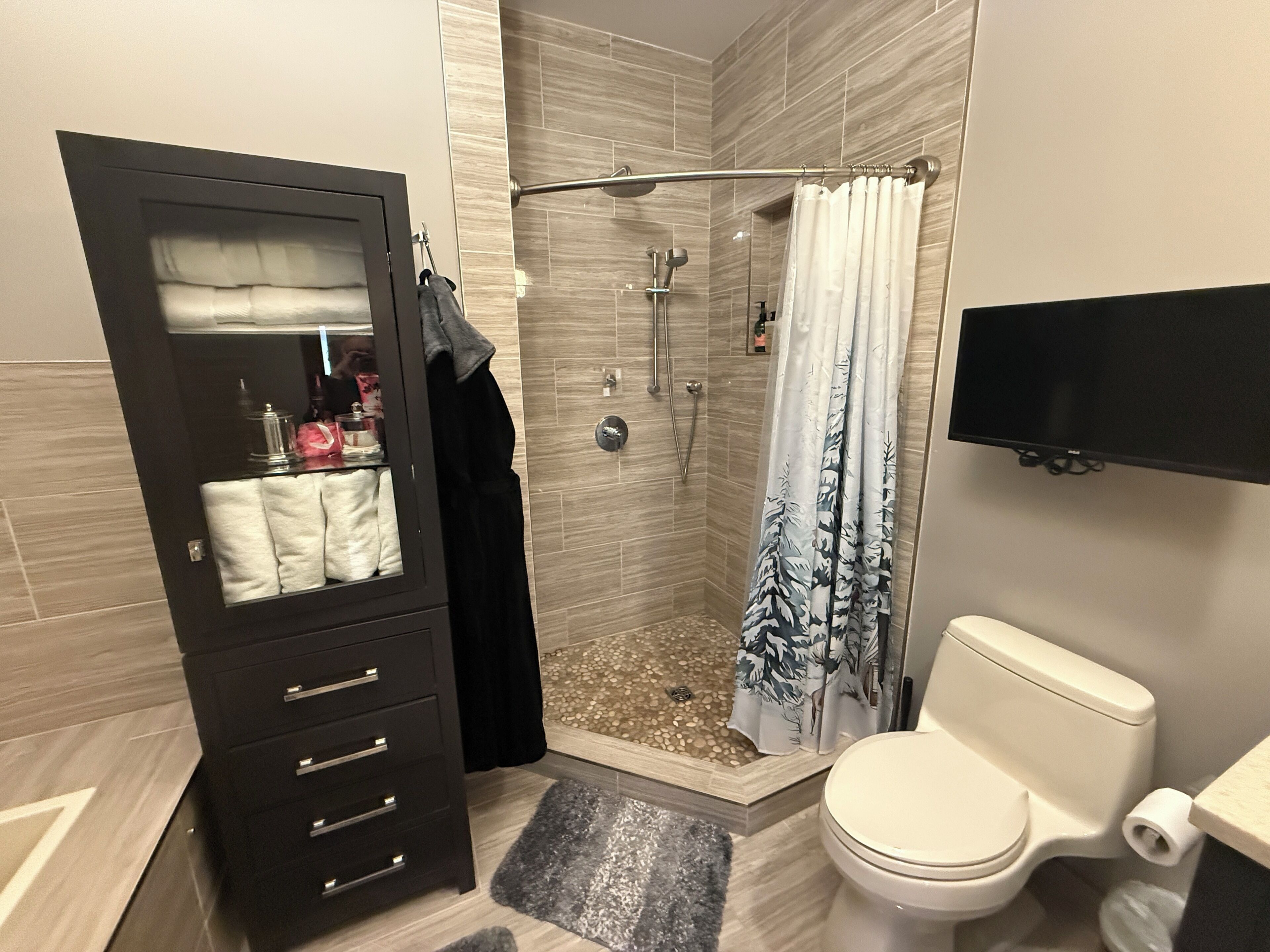 A bathroom with a shower, toilet, and a vanity with a mirror and towel rack.