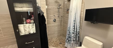 A bathroom with a shower, toilet, and a vanity with a mirror and towel rack.