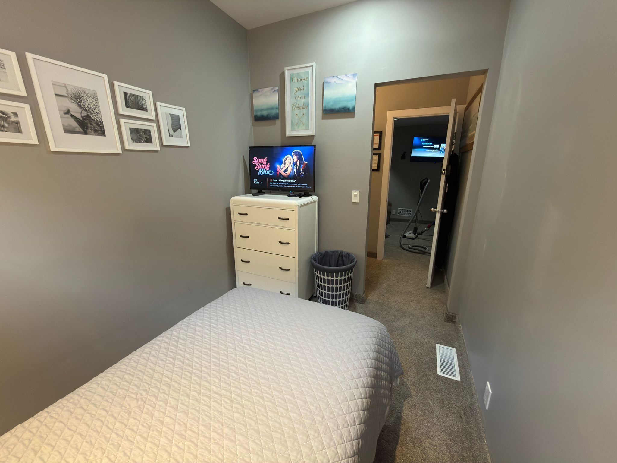 Un dormitorio con cama, cómoda, televisor y pasillo que da a un baño.