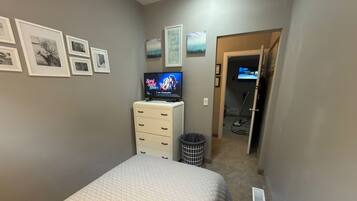 A bedroom with a bed, a dresser, a TV, and a hallway leading to a bathroom.