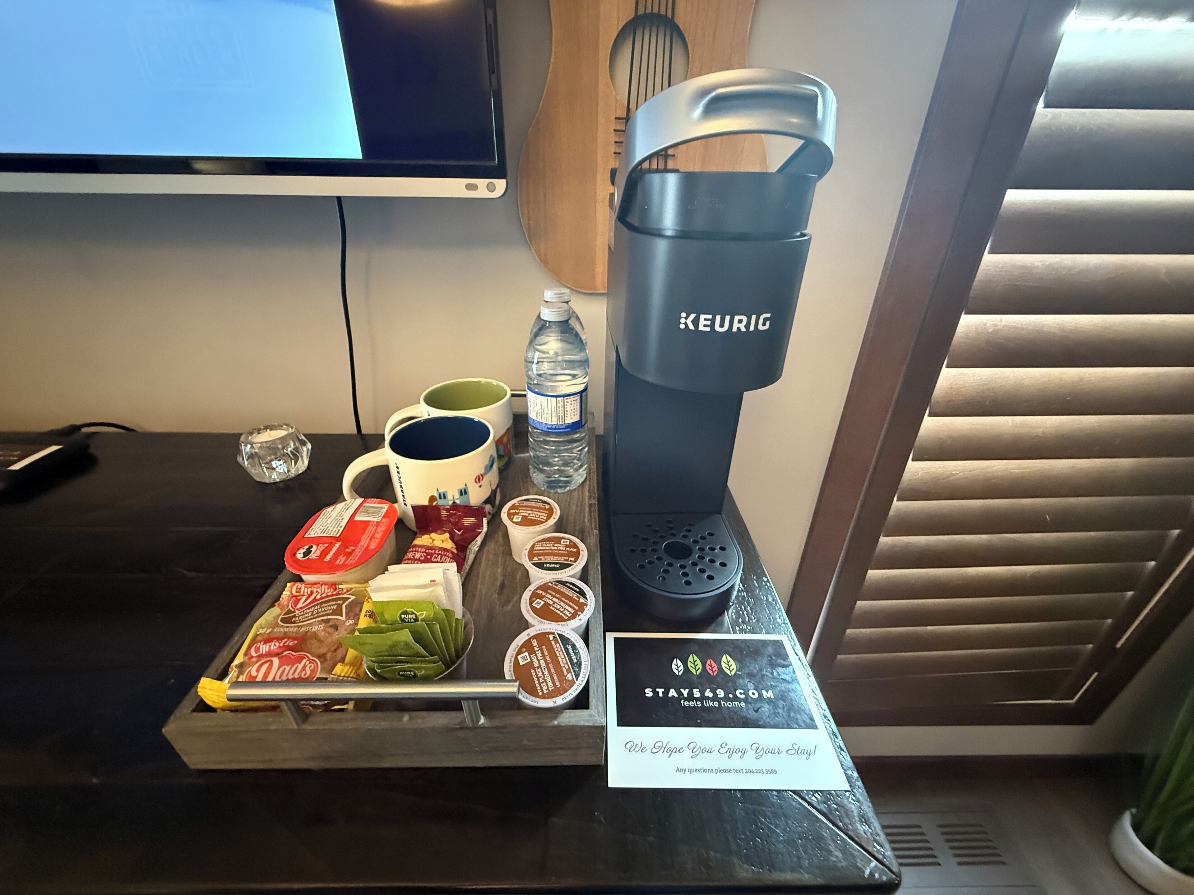 A breakfast tray with coffee maker, water bottle, mugs, and food items.