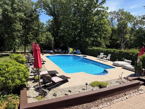 A rectangular swimming pool with lounge chairs and umbrellas, surrounded by trees and greenery. - Stay549 - Adults Only Bed and Breakfast  (Winnipeg)