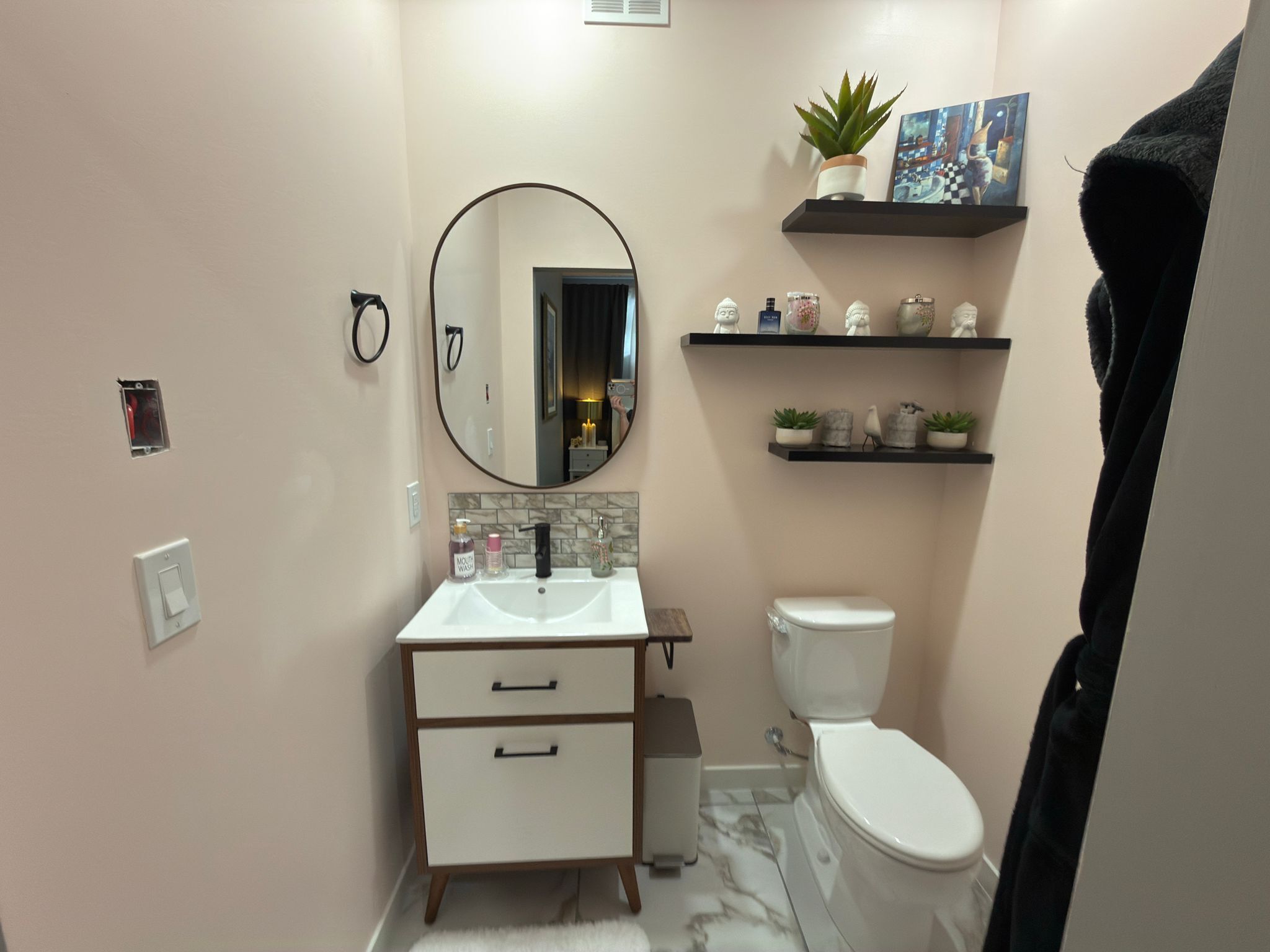 Ein Badezimmer mit einem weißen Waschbecken, einer Toilette, einem Spiegel und Regalen mit Dekoration.