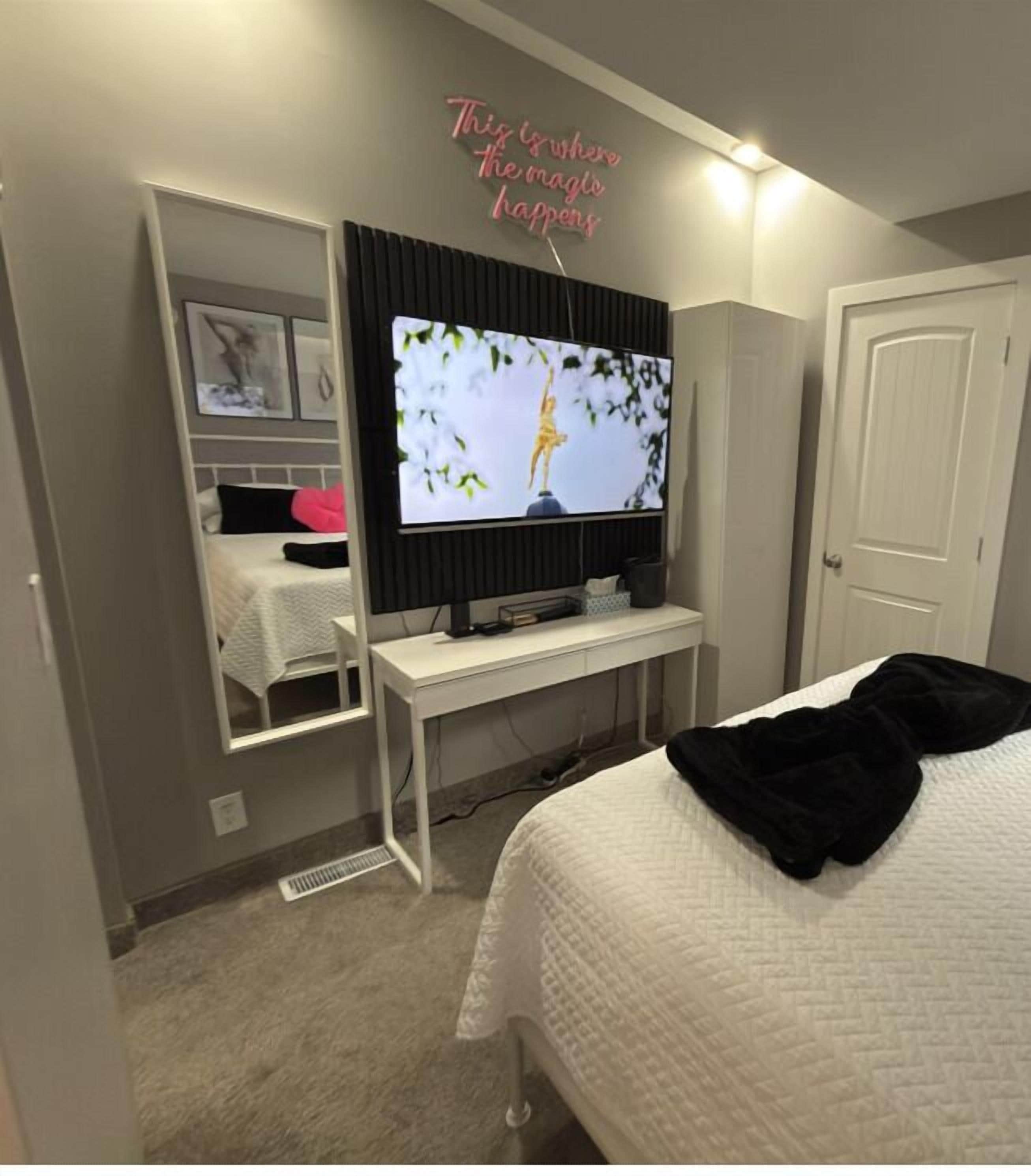 Een slaapkamer met een bed, een televisie op een standaard, een deur en een muur met een motiverende quote.