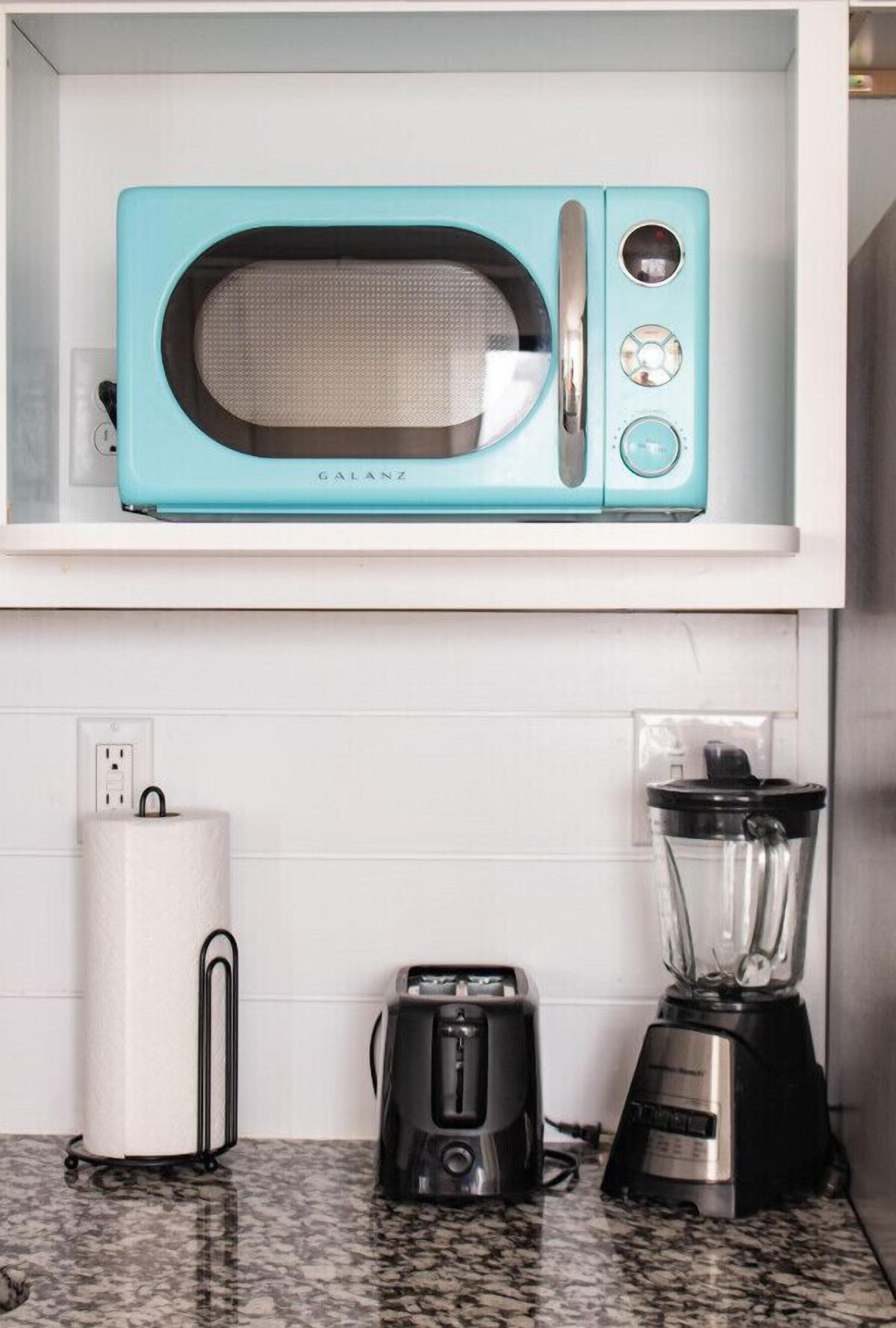Eine Küche mit einer türkisblauen Mikrowelle auf einem weißen Regal, einem weißen Papierhandtuchhalter, einem schwarzen Toaster und einem schwarzen Mixer auf der Arbeitsfläche.