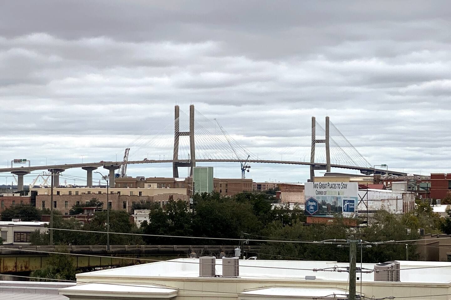 Un puente colgante grande con dos torres, rodeado de edificios industriales y un cielo nublado.