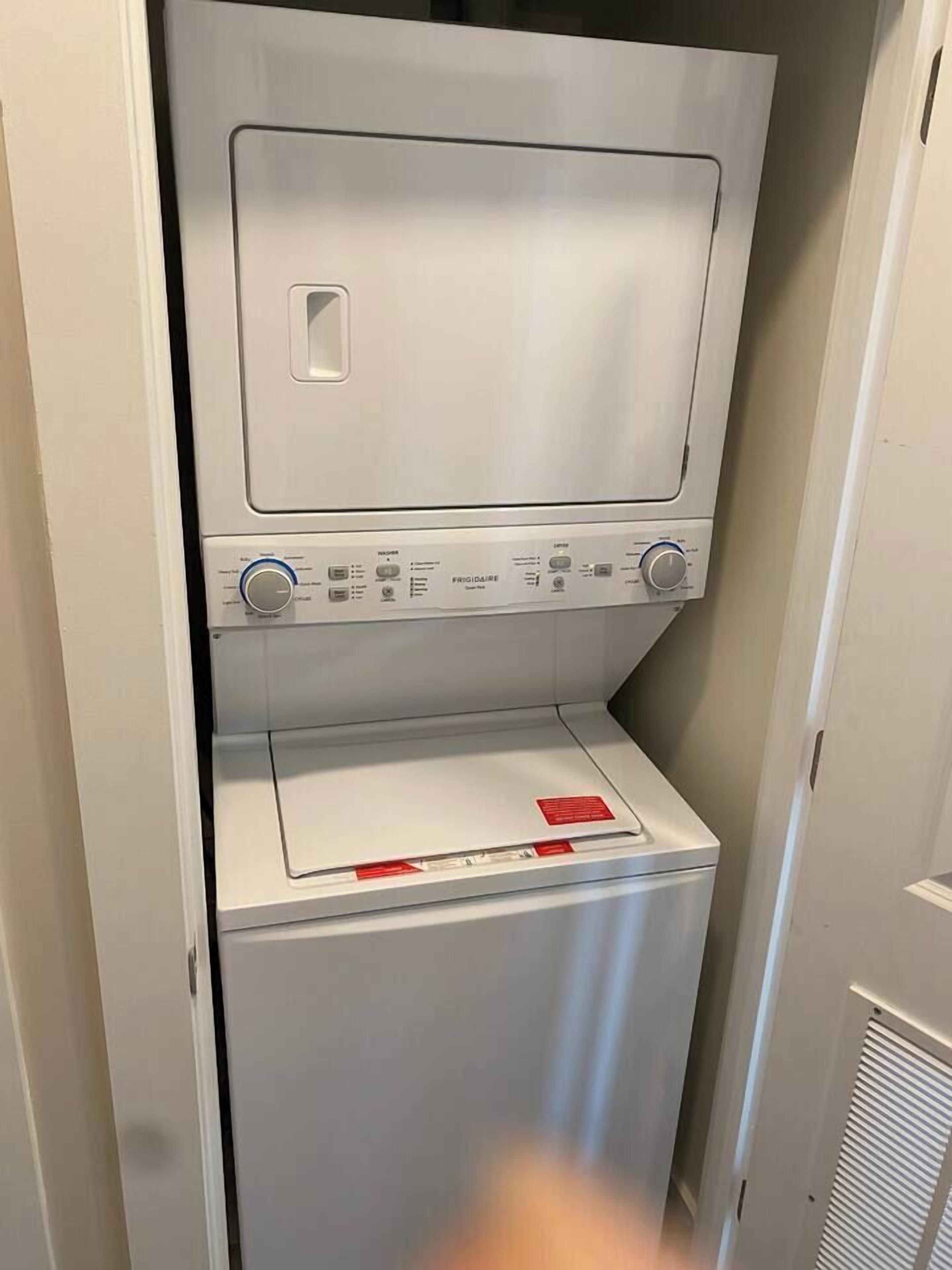 A compact, white, wall-mounted washer and dryer unit with control knobs and a red warning label.