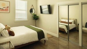 A bedroom with a bed, a bedside table, a mirror, a TV, and a sliding door leading to another room.