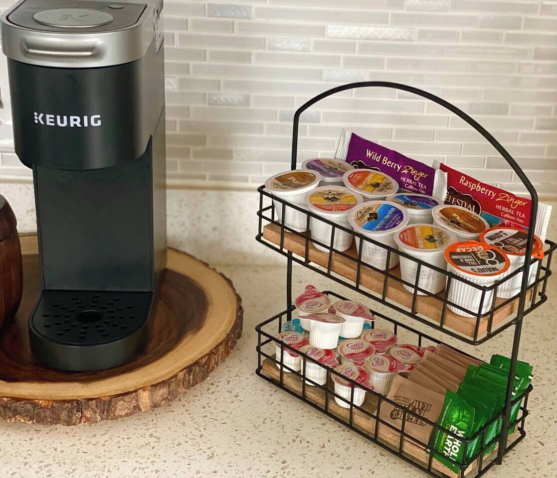 Keurig-kahvinkeitin ja kolmikerroksinen kahvikapseliteline, jossa on useita eri merkkien kahvikapseleita.