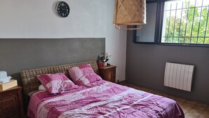 Et soveværelse med seng, sengebord, lampe, vækkeur, et vindue og en radiator.