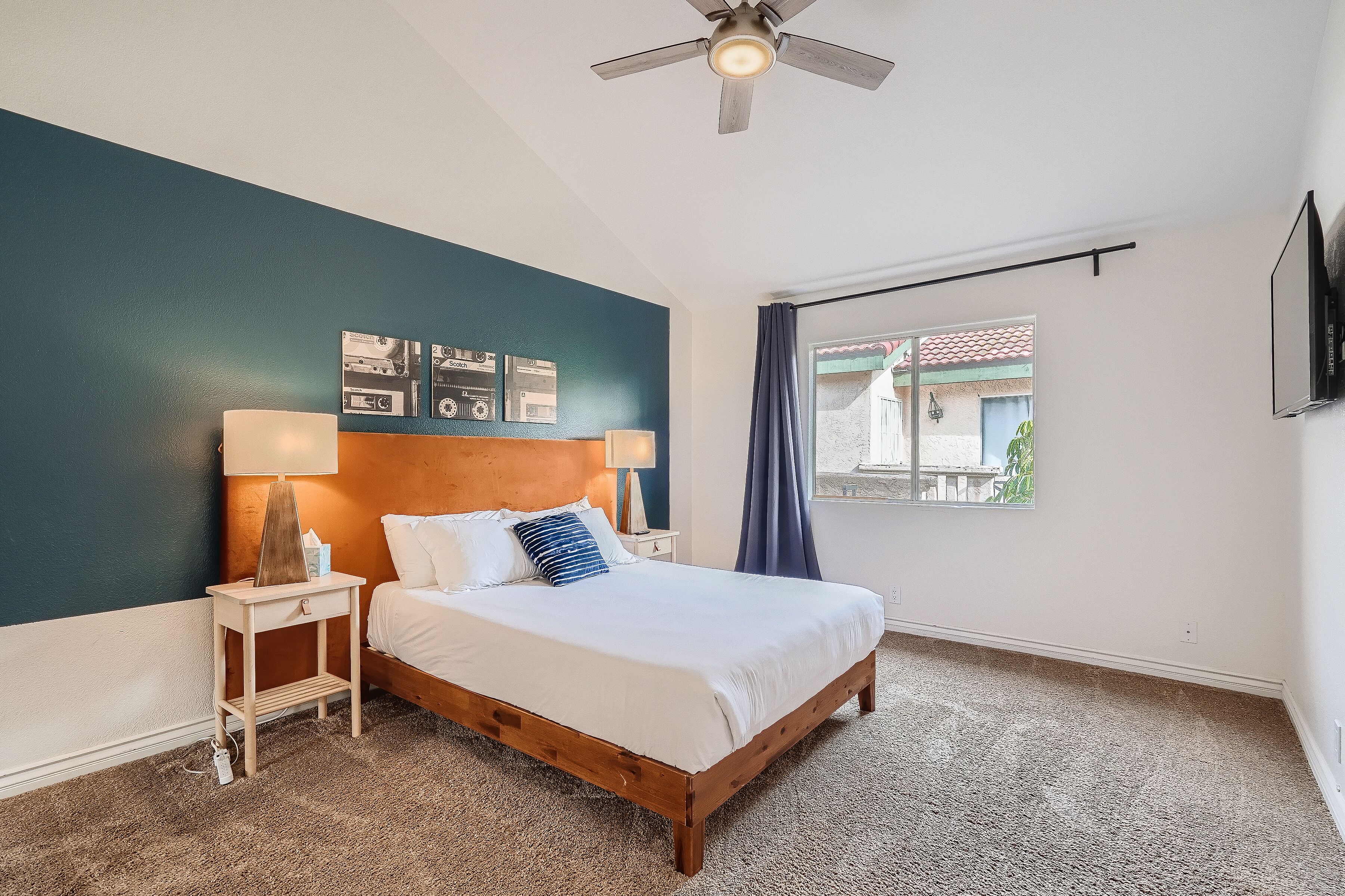 A bedroom with a wooden bed, a nightstand, a ceiling fan, and a window with curtains.