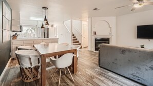A spacious living area with a wooden dining table, white chairs, a grey sofa, a flat-screen TV, and a staircase leading to another level. - 1 Block to Pacific Beach/FOOD/Bars, Updated, 2-Car Garage w/fee, Yard, Sleeps 8! (San Diego)