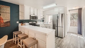 A modern kitchen with white cabinetry, stainless steel appliances, and a bar area with stools. - 1 Block to Pacific Beach/FOOD/Bars, Updated, 2-Car Garage w/fee, Yard, Sleeps 8! (San Diego)