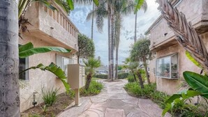 A pathway leading to a building with a stucco exterior, surrounded by tropical plants and palm trees. - 1 Block to Pacific Beach/FOOD/Bars, Updated, 2-Car Garage w/fee, Yard, Sleeps 8! (San Diego)