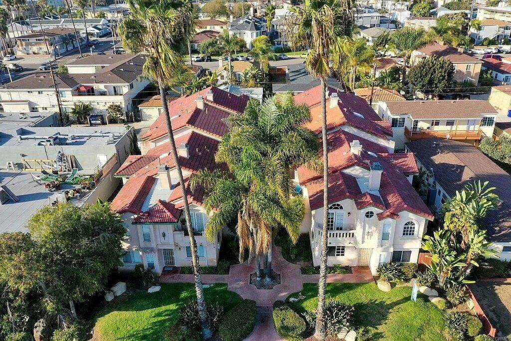 A large, multi-story house with a red-tiled roof, surrounded by palm trees and a well-maintained lawn.